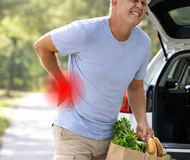 Homme portant un sac de courses qui porte la main à son bas du dos